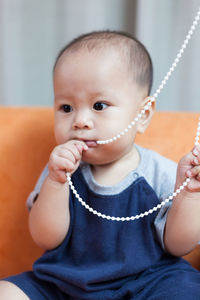 Close-up of toddler biting roller blind chain on sofa at home