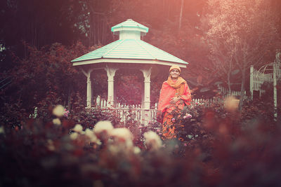 Low angle view of woman standing by building against trees