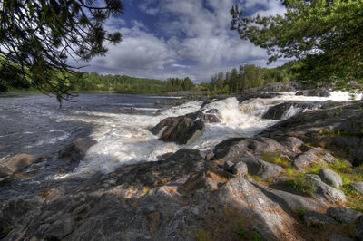 Scenic view of waterfall in forest against sky