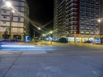 Empty road by illuminated buildings against sky at night