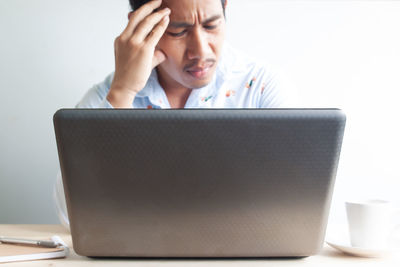 Man with head in hands looking at laptop against wall