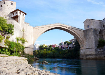 Arch bridge over river amidst buildings against sky