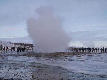 People watching steam on frozen landscape against sky