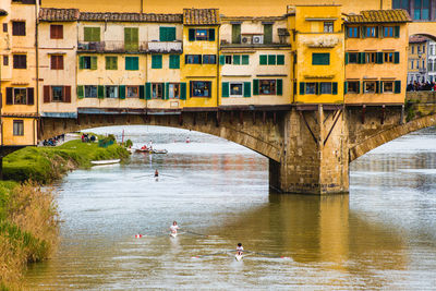 People on bridge over river by buildings in city