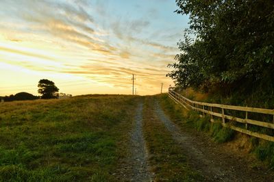 Country road passing through field against cloudy sky