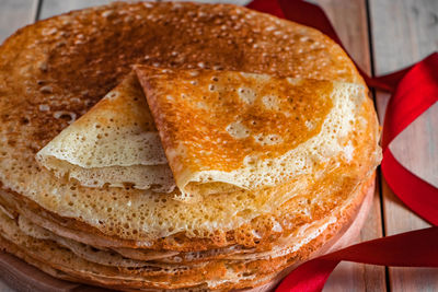 Crepes on a light wooden background and a red ribbon. symbol of the sun, traditional food 