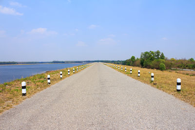 Empty road along calm sea against sky