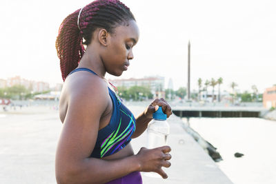 Side view of african american female athlete with bottle of water standing near pier