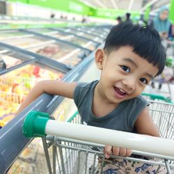 Portrait of smiling boy sitting at shopping cart