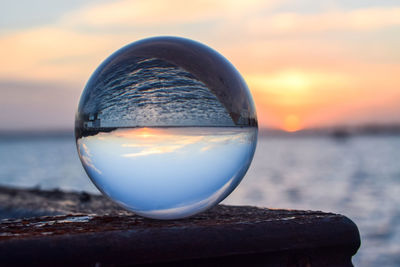 Close-up of crystal ball in sea against sky during sunset