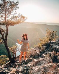 Portrait of woman standing by tree against valley during sunset