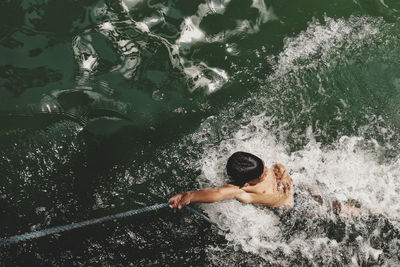 High angle view of shirtless man holding rope swimming in river