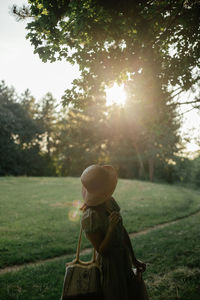 Rear view of woman standing on field against trees