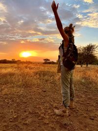 Woman with arms outstretched standing against sky during sunset