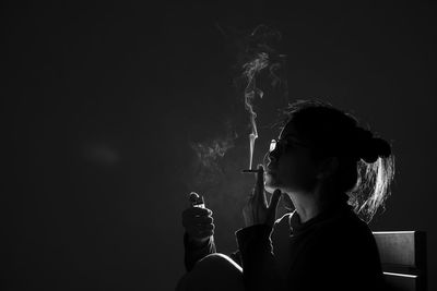 Portrait of man smoking cigarette against black background