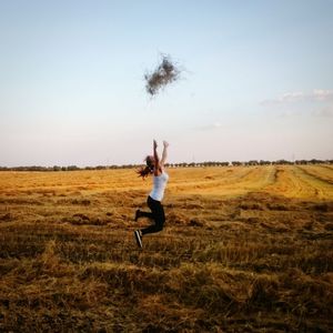 Full length of woman jumping on field against clear sky