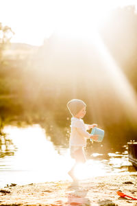 Summer golden sun toddler playing with bucket at lake