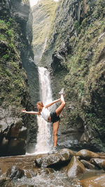 Mid adult woman doing yoga on rock by waterfall
