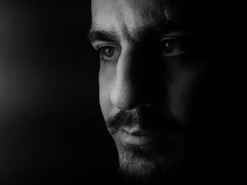 Close-up of young man looking away against black background