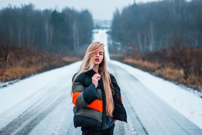 Portrait of young woman standing on snow covered road
