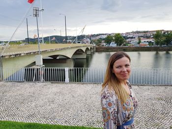 Portrait of beautiful woman standing on bridge over river against sky