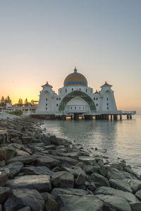 Mosque over sea against sky during sunset