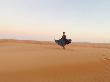 Woman dancing on sand at desert against sky during sunset