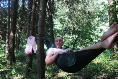 Midsection of man sitting on hammock in forest