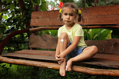 Portrait of cute girl with injured knee sitting on bench