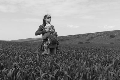 Full length of woman carrying a baby while standing on field