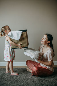 A daughter at home is carrying a basket of washed clothes to her mother