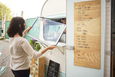 Rear view of female owner opening window at food truck with male colleague