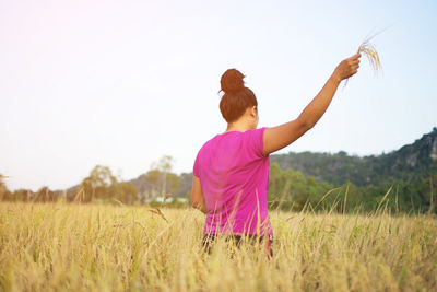 Rear view of woman standing in field against clear sky