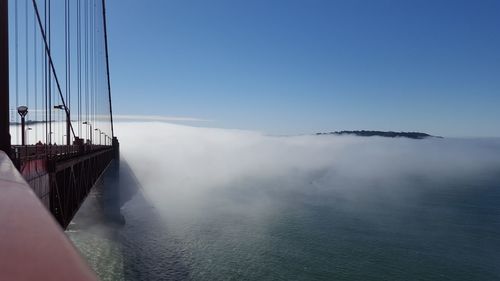 Bridge over sea against clear blue sky during foggy weather