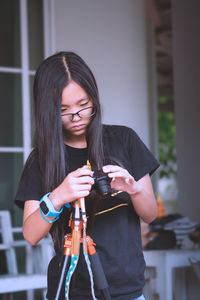 Girl holding camera while standing against house