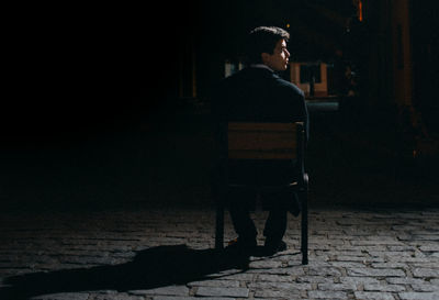 Teenage boy sitting on chair at street during night