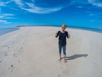 Fish-eye view of smiling man gesturing peace sign while standing on shore at beach against sky