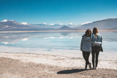 Rear view of female friends standing by lake with reflection