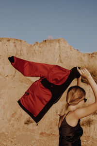 Side view of woman holding jacket against mountain and sky