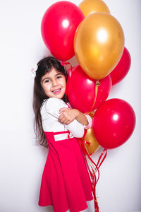 Rear view of smiling girl holding balloons against white background