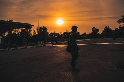 Rear view of silhouette person standing on road against sky during sunset