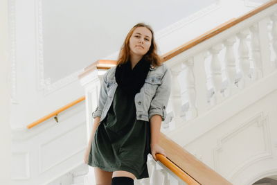 Low angle portrait of young woman standing on staircase at home