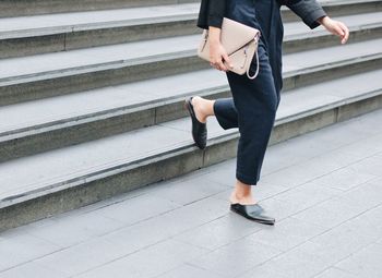 Low section of woman holding purse while moving down on steps