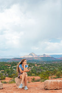 Rear view of woman sitting on mountain against sky