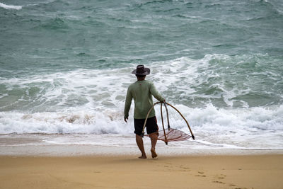 Rear view of man with fishing net walking at beach