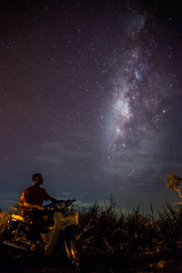 Man riding motor scooter on field against star field