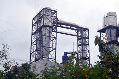 Low angle view of crane by building against sky