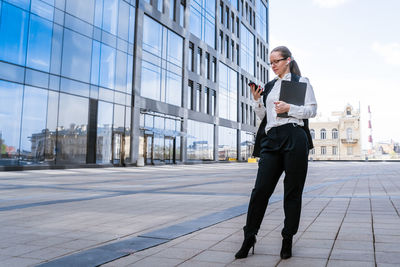 Caucasian business lady in suit holding laptop and talking on phone, posing