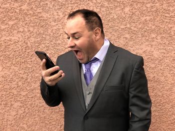 Close-up of businessman using mobile phone against wall