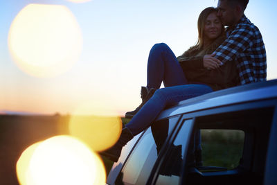 Couple embracing on car roof against sky